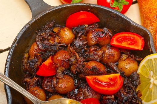 Baby cuttle fish roasted on iron skillet with tomatoes and onions over rustic wood table