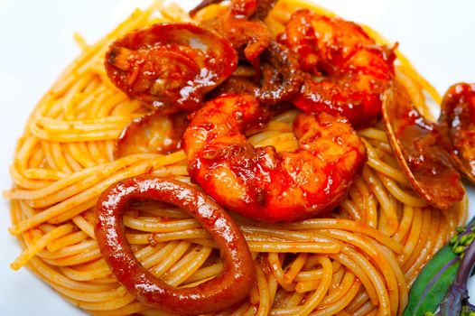 Italian seafood spaghetti pasta on red tomato sauce over white rustic wood table