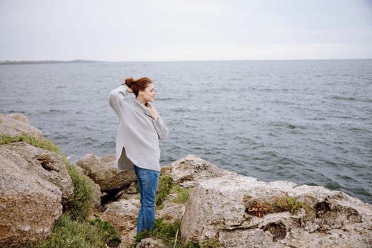 pretty woman in a gray sweater stands on a rocky shore nature Lifestyle. High quality photo