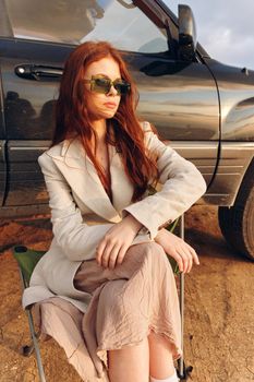 pretty woman in a coat outdoors sitting on a chair near the car endless field. High quality photo