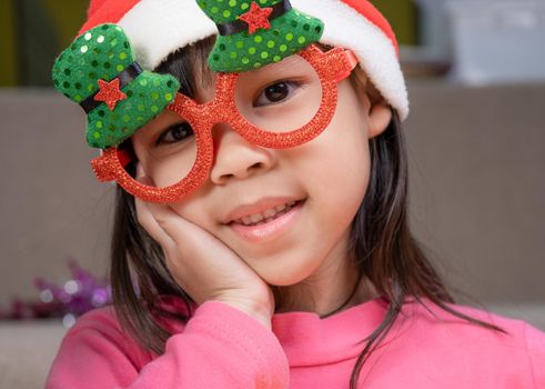 Little girl in a Santa hat sitting on the floor and making wishes near the Christmas tree at home. Happy New Year and Merry Christmas.