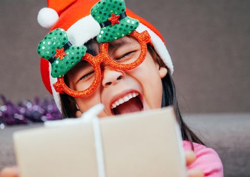 Happy little girl in Santa hat giving a Christmas present at home. Happy New Year and Merry Christmas.