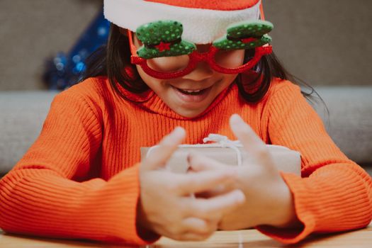 Happy little girl in Santa hat with christmas gift box at home. Happy New Year and Merry Christmas.