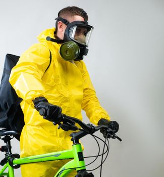 courier delivering food on a bicycle wearing a gas mask and a protective yellow suit