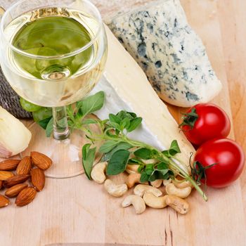 Glass of white wine with cheese nuts and tomatoes on a wooden plate