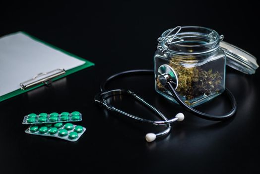 the Dry medical cannabis in a jar with a stethoscope on a black background