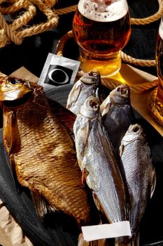 Various appetizing whole air-dried and smoked fish served on black wooden board with foamy amber lager. Popular complements to beer concept