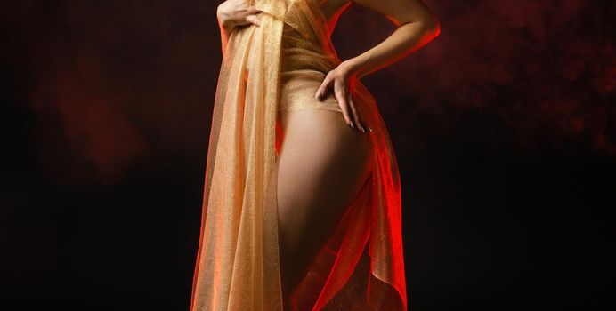 Young nude woman posing in studio with a golden shawl on a dark background