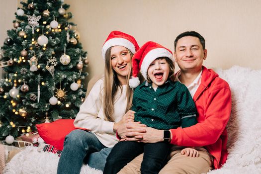 Portrait of happy smiling family with kid son. Laughing mother in Santa hat, father, child boy in sweater having fun on Christmas holidays at home. Merry Christmas and happy new year.
