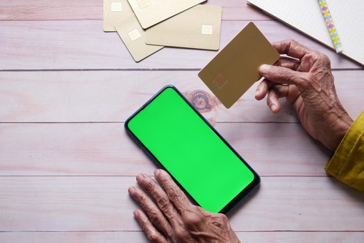 senior women hand holding credit card and using smart phone shopping online .
