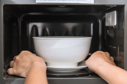 People putting food ceramic bowl in to the Microwave for reheating food.