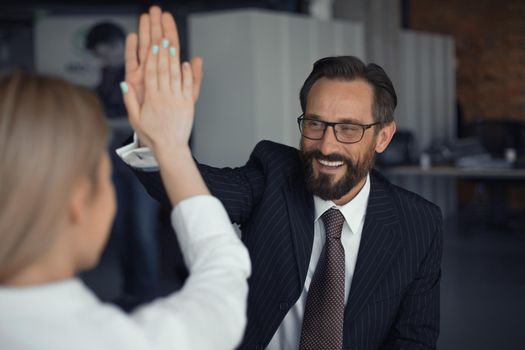 Happy Successful Businessman giving high five with businesswoman standing back in foreground. Teamwork concept.