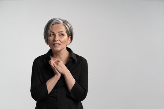 Portrait of a mature business woman looking wondered sideways.Pretty mid aged grey haired woman in black shirt isolated on grey background. Human emotions, facial expression concept.