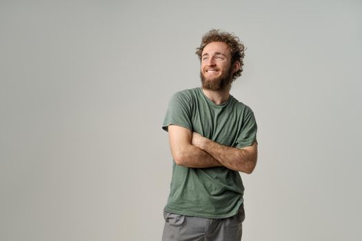 Portrait of smiling young man with hands folded. Handsome young man with curly hair in olive t-shirt looking at camera isolated on white background.