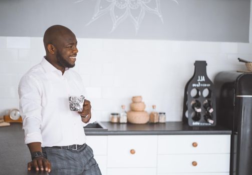 Sincerely Meeting In Kitchen. Happy African-American With Cup Looks Away. Meeting Friends Of Successful Businessman At Home. High quality photo