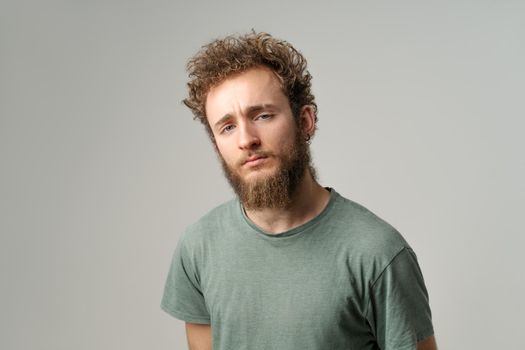 Interrogatively persistent gaze of a handsome young man with curly hair in olive t-shirt isolated on white background. Portrait of smiling young.