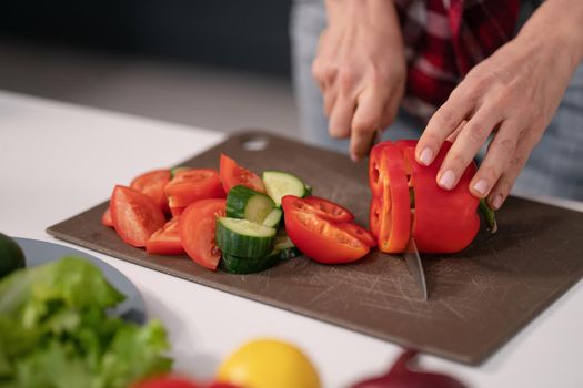 Cuts vegetables for a fresh salad young housewife cut bell pepper, cucumber, tomato on cutting board preparing for a family dinner standing in the new kitchen of a new home. Healthy lifestyle.