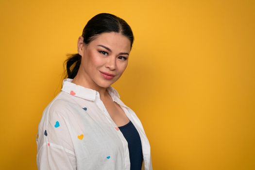 Asian mature woman wearing casual posing in studio. Smiling female brunette isolated on yellow background.