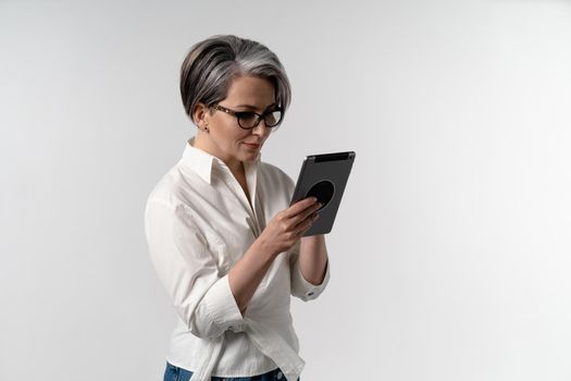 Senior grey haired woman in white shirt using digital tablet. The use of technology by the elderly browsing internet shopping online on pad isolated on white background.