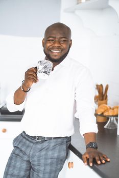 Successful Young Businessman. African American Man Stands With Cup In His Kitchen. He Is Happy And Smiling. Concept Of Luxurious, Rich Life. High Quality Photo