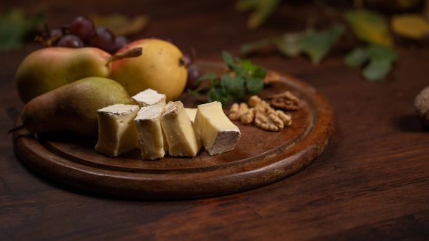 Snacks set: cheese, grapes, pear and three walnuts on a wooden table. Brie cheese with fruits, grapes, walnuts on a dark wooden plate and wooden board.