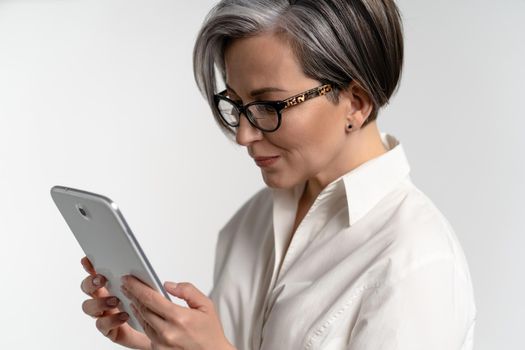 Close up. Senior grey haired woman in white shirt using digital tablet. The use of technology by the elderly browsing internet shopping online on pad isolated on white background.