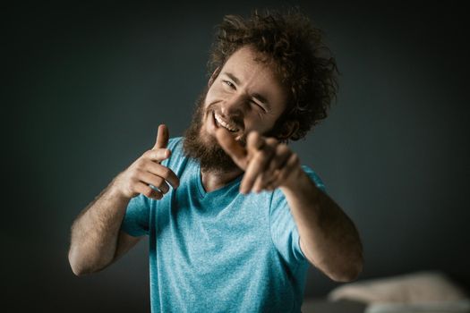 Cheerful Guy in a Blue T-shirt with Happy Eyes and a Wide Smile Points his Fingers to the Camera. Close-up Portrait. Grey Background. High quality photo