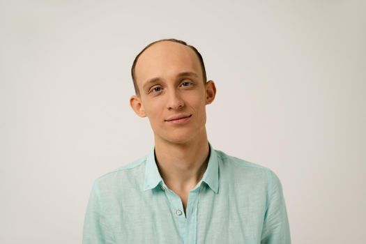 Portrait of young bald man with funny protruding ears in coral blue shirt with looking at camera isolated over white background in studio. Hair loss concept.