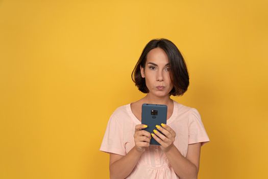 Serious young woman with mobile phone. Millennial lady using app, reading message in her smartphone. Cut out on yellow background. Copy space. High quality photo