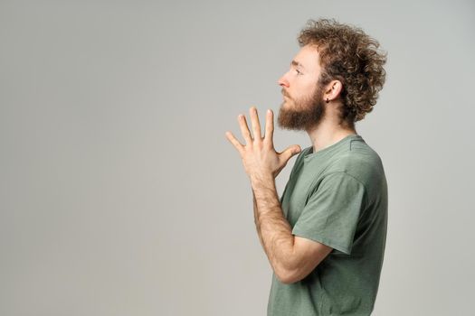 Young handsome man casual sideways pose with palms folded. Handsome young man with curly hair in olive t-shirt looking at camera isolated on white background.