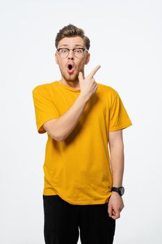 Handsome young man pointing finger sideways in eye glasses shocked with surprise expression on his face.Young casual man portrait isolated on yellow background.