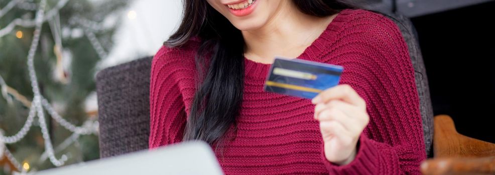 Young asian woman online shopping in Christmas with credit card on laptop computer, female buying and payment with debit card, xmas in holiday, happy new year, customer with purchase to internet.