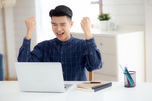 Happy young businessman work on laptop computer finish with excited and success on desk at home, business man using notebook with achievement and surprised, freelance or employee, satisfied and glad.