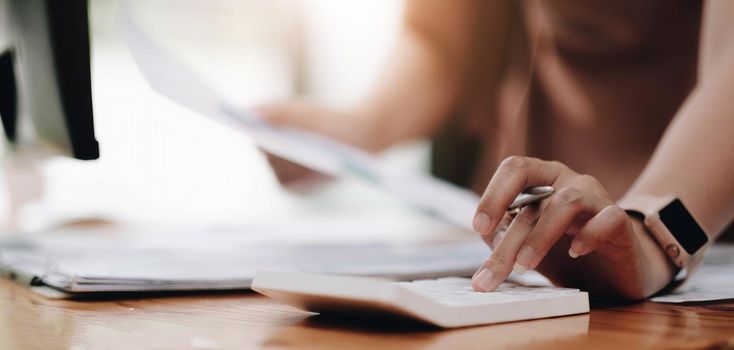 Close up woman using calculator and laptop for do math finance on wooden desk in office and business working background, tax, accounting, statistics and analytic research concept.