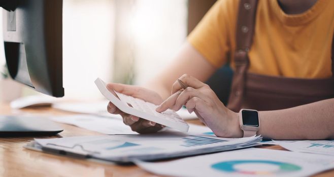 Close up woman using calculator and laptop for do math finance on wooden desk in office and business working background, tax, accounting, statistics and analytic research concept.