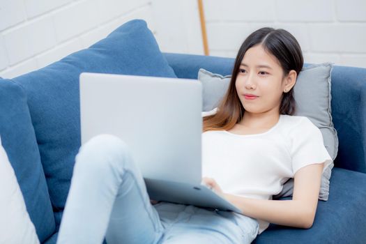 Young asian business woman smile and work from home with laptop computer online to internet on sofa in living room, freelance girl using notebook on couch with comfort, new normal, lifestyle concept.