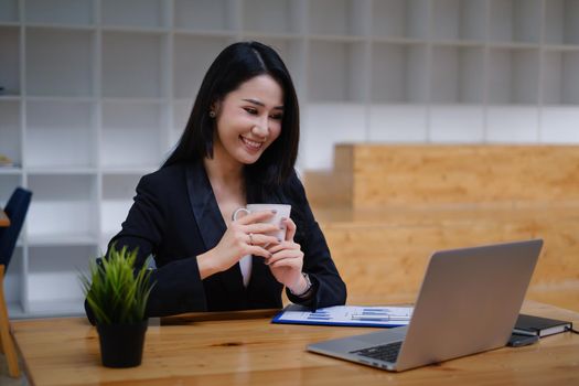 Cheerful young asian woman using laptop computer at home. Student female in living room. online learning, studying , online shopping, freelance, asean concept.