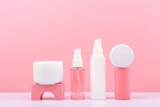 Trendy composition in pink colors with set of cosmetic bottles with beauty products on geometric props against pink background. Concept of organic cosmetics for glowing, young looking skin