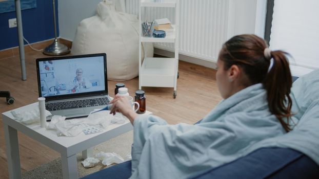 Sick patient talking to doctor on video call for telehealth with laptop. Woman showing thermometer with temperature measurement to medic on online conference, asking for treatment against fever