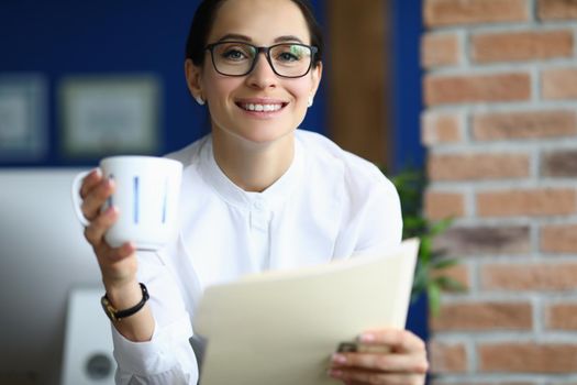 Portrait of attractive brunette businesswoman at work with cup of coffee read report. Smiling positive energy from boss. Business, morning routine concept