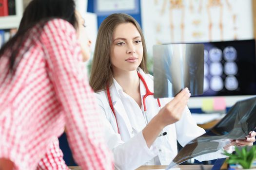 Portrait of clever professional doctor examine x ray result on appointment, show patient. Medical worker describe scan to client. Health, checkup concept