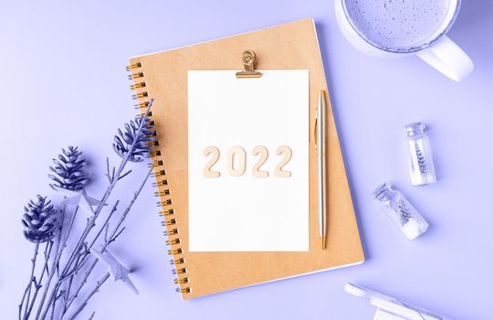 Top view Desktop Christmas notepad with 2022 text in color of year. Flat lay table background with planner, cup of coffee, tree brunch, Christmas eco nature decoration, notebook and stationery.