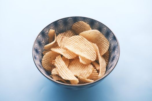 Bowl with tasty potato chips on wooden background
