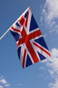 UK Great Britain national flag hanging on flagstaff over cloudy blue sky, symbol of British patriotism, low angle, side view