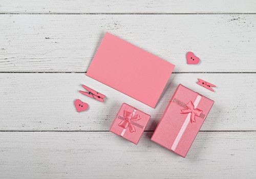 Valentine template of pink gift boxes with ribbon chiffon bows and paper note on white wooden table background, close up flat lay, elevated top view, directly above