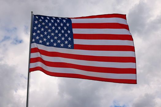US national flag flying and waving in the wind over gray stormy cloudy sky, symbol of American patriotism, low angle, side view