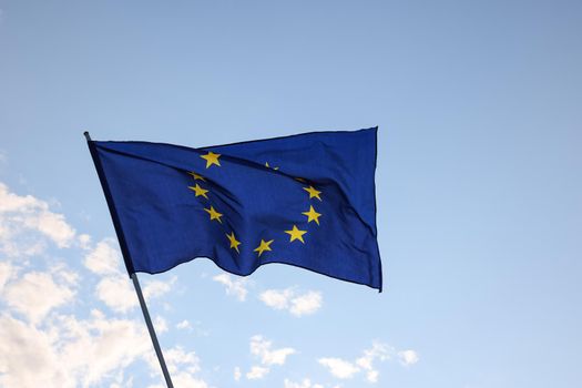 European Union EU flag flying and waving in the wind over clear blue sky, symbol of European patriotism, low angle, side view