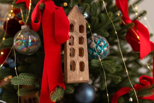 Beautiful decorated christmas tree, red ribbons, balls, wooden house. Merry Christmas and New Year holidays background.