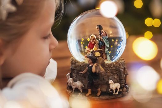 Girl looking at a glass ball with a scene of the nativity of Jesus Christ in a glass ball