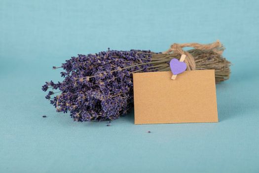 Close up bouquet of dried lavender flowers and small brown paper note on blue tablecloth, high angle view